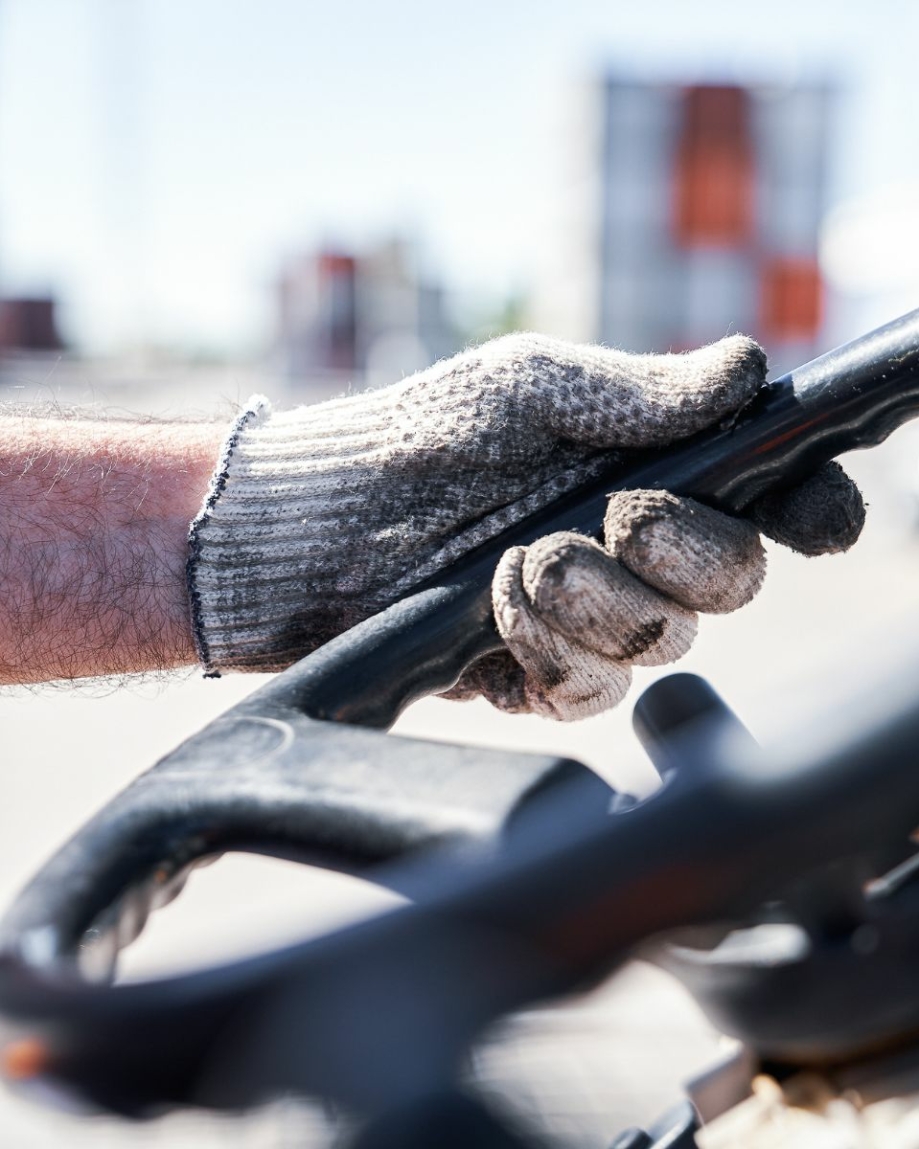 A close up image of a dirty white gloved hand holding a steering wheel on a forklift.