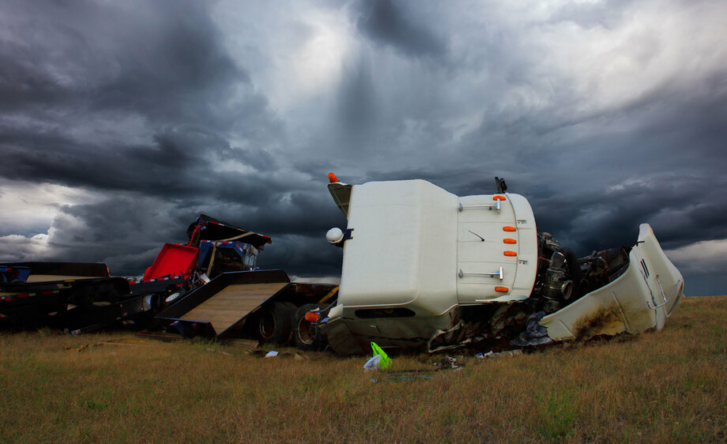 A photo of the wreckage of a white cargo truck on its side, with a stormy sky behind it.
