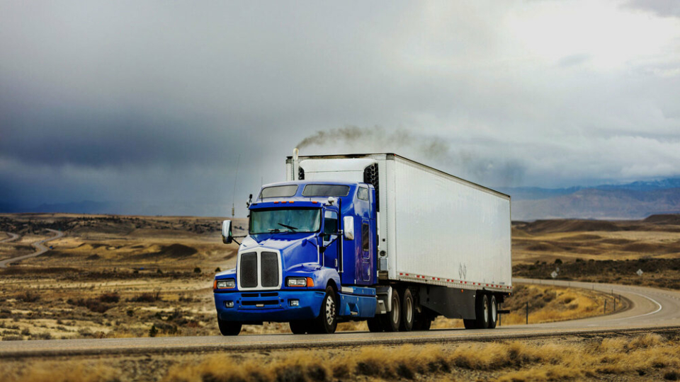 A photo of a truck with a blue cabin and white unit, driving through the countryside.