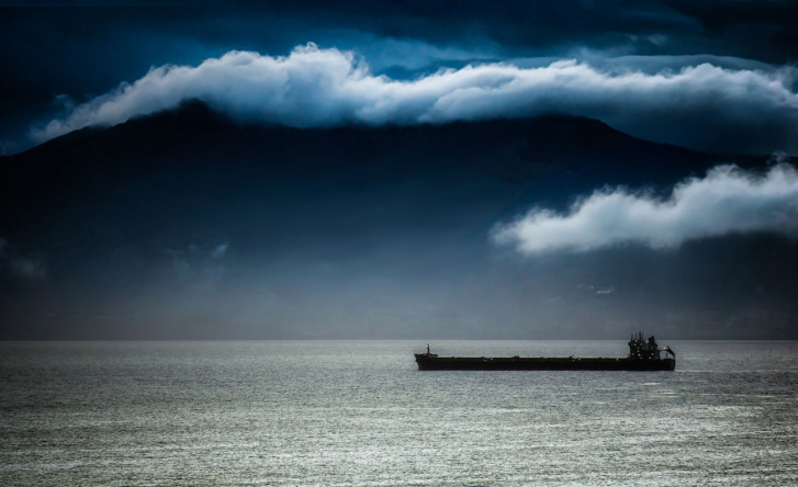 A landscape photo of a stormy sea with clouds hanging over it, and one cargo boat floating in the middle