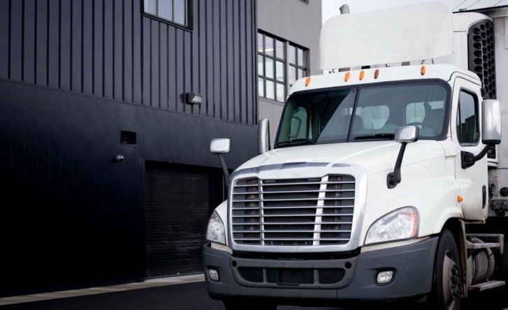 A white cargo truck parked next to a black and grey building on the left.
