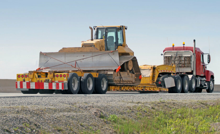 An image of a bulldozer on top of a cargo truck, being towed away